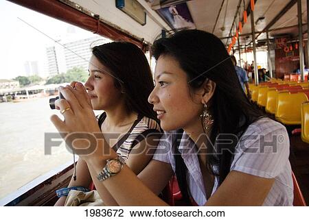 Stock Image - Thailand, Bangkok, Thai Women Take A Photo Out The Window Of A Boat.. Fotosearch