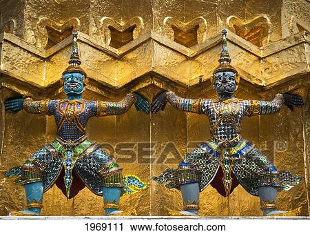 Stock Image - Thailand, Bangkok, Wat Phra Kaew, Guardian Mythical Demons Or Yaksha Support The Base Of A Golden Chedi At Wat Phra Kaew On The Grounds Of The Grand Palace.. Fotosearch
