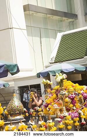 Stock Image - Thailand, Bangkok, Woman Praying By Flowered Altar; Erawan Shrine. Fotosearch