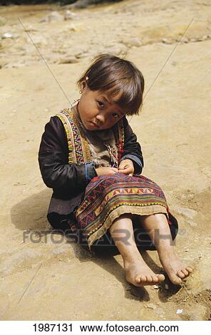 Stock Image - Thailand, Chiang Mai, Young H'mong Girl, Sitting On Rocks, In Traditional Attire. Editorial Use Only.. Fotosearch