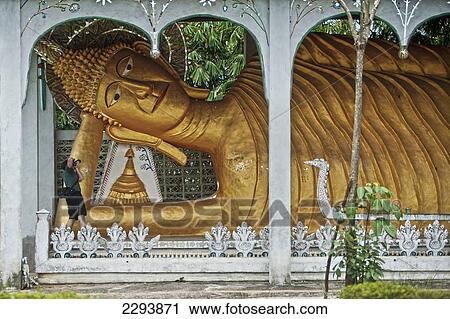Stock Image - Thailand, Kanchanaburi, Sangkhlaburi, Tourist taking photograph of Reclining Buddha; Wat Somdet. Fotosearch