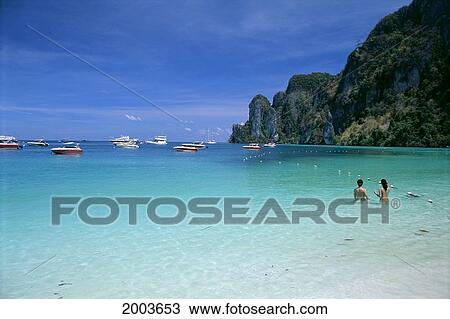 Stock Image - Thailand, Koh Pee Pee, Couple Swimming In Coastal Waters, Boats In Background. Fotosearch