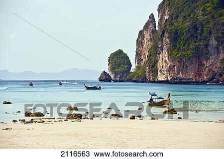 Stock Image - Thailand, Koh Phi Phi, Longtail boats along the shoreline, Mountains in distance.. Fotosearch