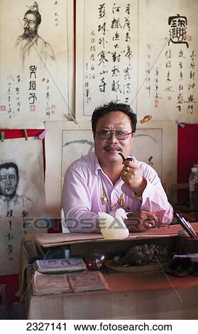 Thailand, Man smoking pipe while sitting at desk in Chinese village near Pai; Shandicun View Large Photo Image Stock Image - Thailand, Man smoking pipe while sitting at desk in Chinese village near Pai; Shandicun. Fotosearch