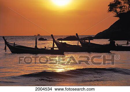 Picture - Thailand, Phuket, Fishing Boats Tied Near Shoreline, Golden Orange Sky, Large Boat Horizon. Fotosearch