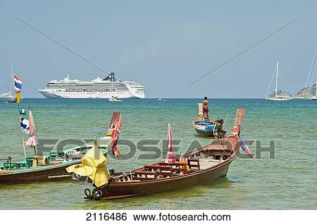 Stock Photograph - Thailand, Phuket, Patong, Longtail boats along the shoreline, Cruiseship in distance.. Fotosearch