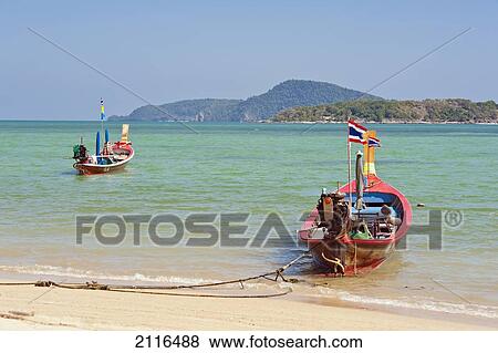 Stock Photo - Thailand, Phuket, Rawaii Beach, Longtail boats along the shoreline, Land in distance.. Fotosearch