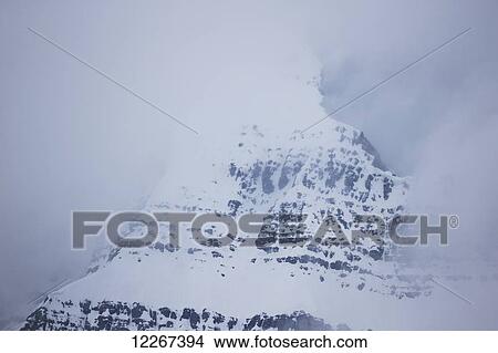Picture - The fog shrouded peak of a mountain peaks through the clouds, Jasper National Park; Alberta, Canada. Fotosearch