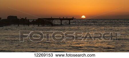 Stock Image - The golden sun sinking behind the water at sunset with orange sky; Paphos, Cyprus. Fotosearch