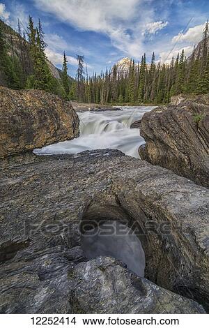 Picture - The Kicking Horse River flows over a waterfall before it goes beneath a natural bridge, Yoho National Park; British Columbia, Canada. Fotosearch