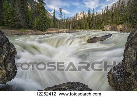 Stock Image - The Kicking Horse River flows over a waterfall before it goes beneath a natural bridge, Yoho National Park; British Columbia, Canada. Fotosearch