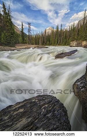 Stock Image - The Kicking Horse River flows over a waterfall before it goes beneath a natural bridge, Yoho National Park; British Columbia, Canada. Fotosearch
