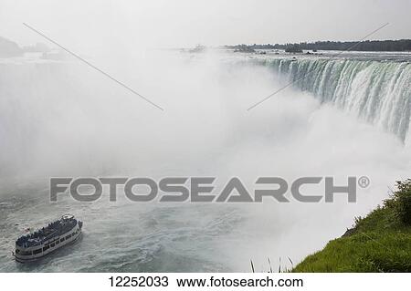 Stock Image - The Maid of the Mist boat at the base of the Horseshoe Falls with large amount of mist; Niagara Falls, Ontario, Canada. Fotosearch