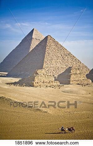 Stock Photograph - The Pyramids With Two Men On Camels Going By; Cairo, Egypt, Africa. Fotosearch