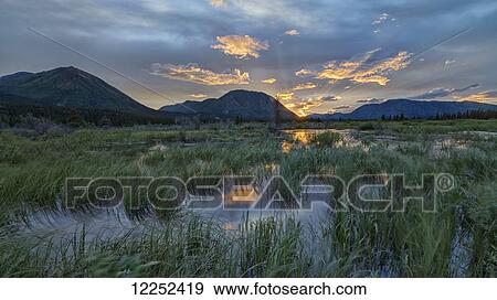The sun sets and creates bands of light behind Toad Mountain near Annie Lake; Whitehorse, Yukon, Canada View Large Photo Image Stock Photo - The sun sets and creates bands of light behind Toad Mountain near Annie Lake; Whitehorse, Yukon, Canada. Fotosearch