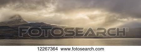 Picture - The sun shines through the storm clouds created beautiful rays of sunshine near the abandoned village of Djupavik; Iceland. Fotosearch