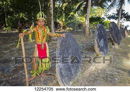 Stock Photography - This young boy in a traditional outfit is pictured in front of a row of stone money; Yap, Micronesia. Fotosearch