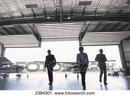 Stock Image - Three businessmen entering airplane hangar; Langley, British Columbia, Canada. Fotosearch