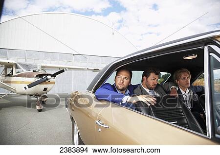 Picture - Three businessmen sitting in the backseat of a car by an airplane; Langley, British Columbia, Canada. Fotosearch