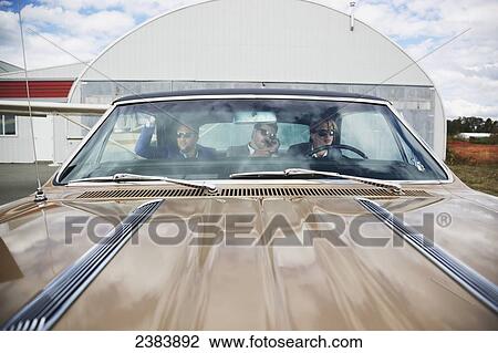 Stock Image - Three businessmen sitting in the backseat of a car by an airplane hangar; Langley, British Columbia, Canada. Fotosearch