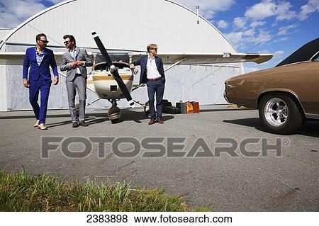 Stock Photo - Three businessmen walking away from a car and airplane hangar; Langley, British Columbia, Canada. Fotosearch