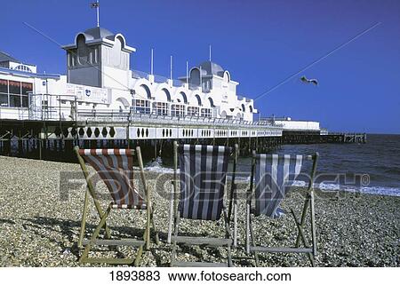 Stock Image - Three Deckchairs On The Beach By Pier. Fotosearch