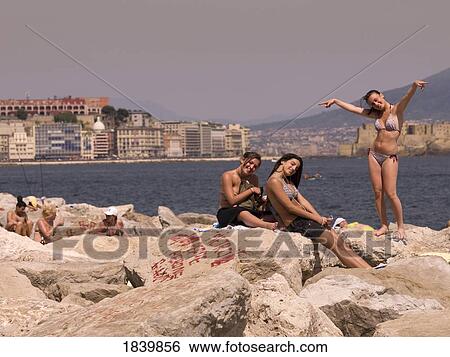 Stock Photograph - Three Girlfriends In Bikini On Shore Rocks; Naples, Italy. Fotosearch