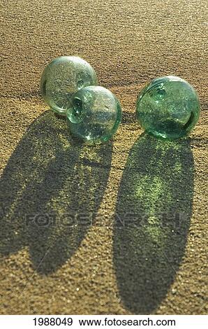 Stock Photo - Three Glass Fishing Floats Rest On Sandy Beach, Afternoon Light Casts Long Green Shadows Through Them. Fotosearch