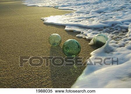 Stock Photography - Three Glass Fishing Floats Rolling Along The Sandy Shoreline. Fotosearch