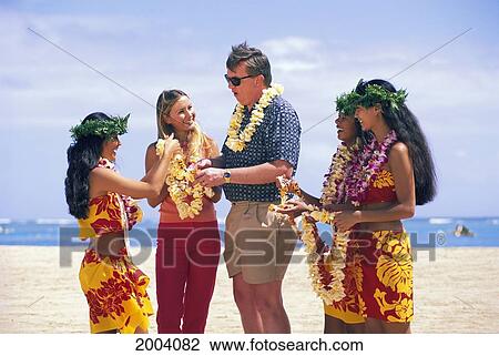 Stock Image - Three Local Women Share Leis With Couple, Beach Scene Colorful Smiling People. Fotosearch