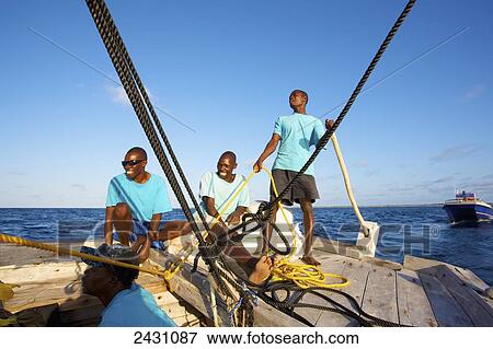 Stock Photo - Three men working together on a sailboat; Vamizi Island, Mozambique. Fotosearch