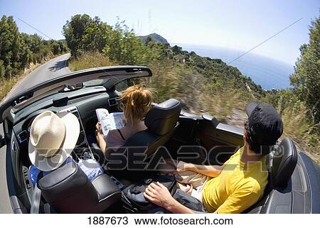 Stock Image - Three People In Convertible Driving By Sea. Fotosearch