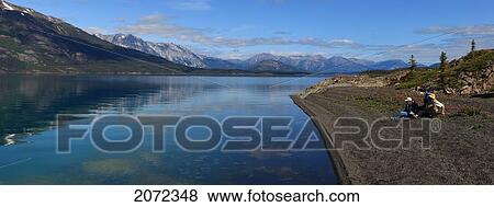 Stock Photo - Three People Sitting On The Shore Of Atlin Lake, Atlin Provincial Park, British Columbia, Canada. Fotosearch