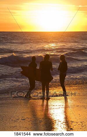Picture - Three Surfers Standing On Beach During Sunset At San Clemente Beach; San Clemente, Orange County, California, Usa. Fotosearch