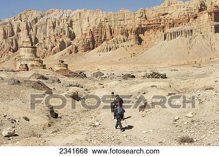 Stock Photo - Three Trekkers Climbing Towards Chortens (Stupas) In Lo Ghekar With Dhakmar Cliffs; Upper Mustang Valley, Nepal. Fotosearch
