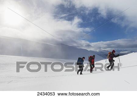 Stock Image - Three walkers on snowy, winter walk ascending Geal Charn, near Laggan; Scotland. Fotosearch