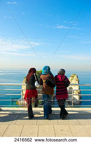Stock Image - Three women stand at a railing looking out over the water; Beirut, Lebanon. Fotosearch