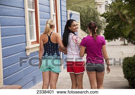 Stock Image - Three Young Female Friends Walking Arm In Arm; California, Usa. Fotosearch