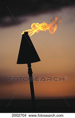Tiki Torch Lit Against Moody Orange And Gray Sunset Skies, Close-Up View Large Photo Image Picture - Tiki Torch Lit Against Moody Orange And Gray Sunset Skies, Close-Up. Fotosearch