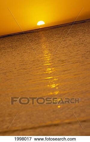 Stock Photo - Tilted View Of Half Sunball Along Horizon, Orange Sunset Sky With Reflections On Ocean. Fotosearch