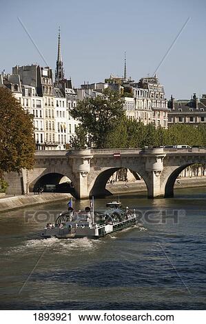 Stock Image - Tour Boat Along The River With Bridge And Building In The Background; Paris, France. Fotosearch