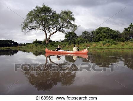 Stock Photography - Tourist and tour guide ride in a boat down a tranquil river, Lower Zambezi National Park; Zambia. Fotosearch