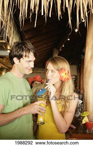 Stock Image - Tourist Couple At An Island Style Bar Enjoying Cocktails. Fotosearch