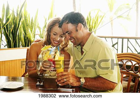 Stock Image - Tourist Couple At An Island Style Bar Enjoying Cocktails. Fotosearch