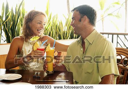 Stock Image - Tourist Couple At An Island Style Bar Enjoying Cocktails. Fotosearch