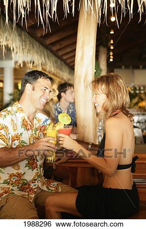Stock Photograph - Tourist Couple At An Island Style Bar Enjoying Cocktails. Fotosearch