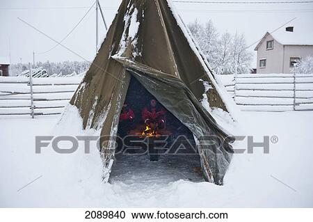 Stock Image - Tourist In Front Of The Fire In Kota Saami Under The Wooden Tepee, Levi, Lapland, Finland. Fotosearch