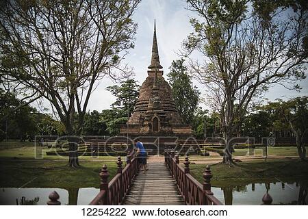 Stock Image - Tourist peers over a bridge in Sukhothai, Thailand's ancient former capital; Sukhothai, Thailand. Fotosearch