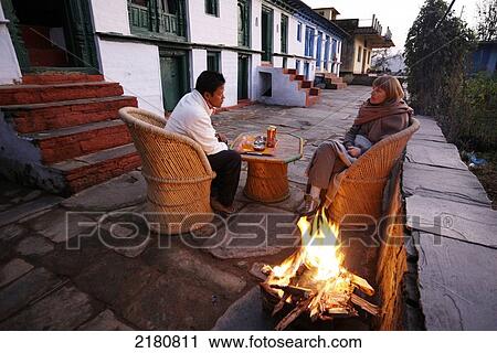 Stock Image - Tourist sits by the fire at dusk while trekking through the himalayas; India. Fotosearch