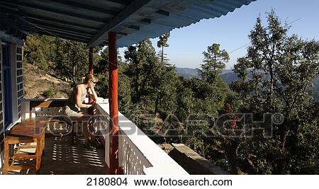 Picture - Tourist sits on a balcony looking at the view of the landscape, Himalayas; India. Fotosearch